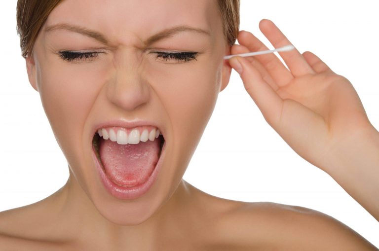 Woman sticking a qtip into her ear with a painful reaction on her face