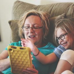 woman and young girl sitting in a recliner while playing with a tablet