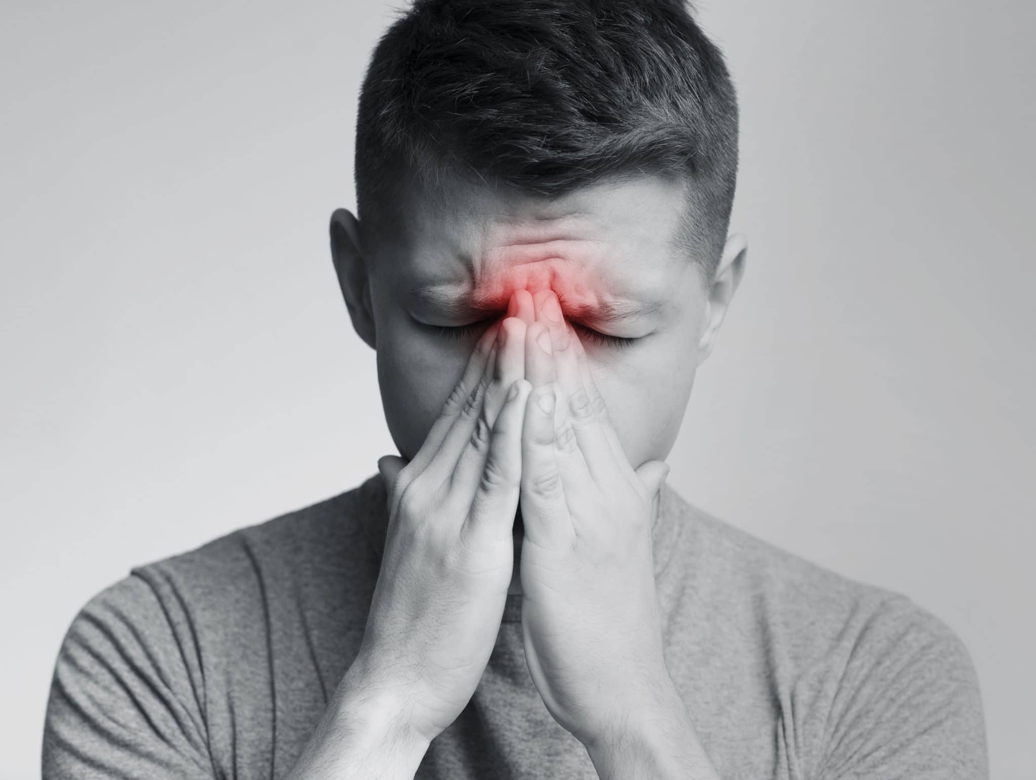 Sinus pain, sinusitis. Sad man holding his nose, black and white photo with red sore zone