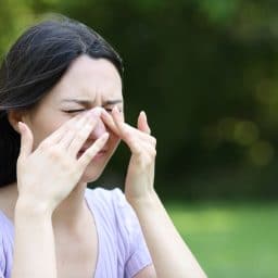 A woman experiencing sinus pressure outside, holding her nose.