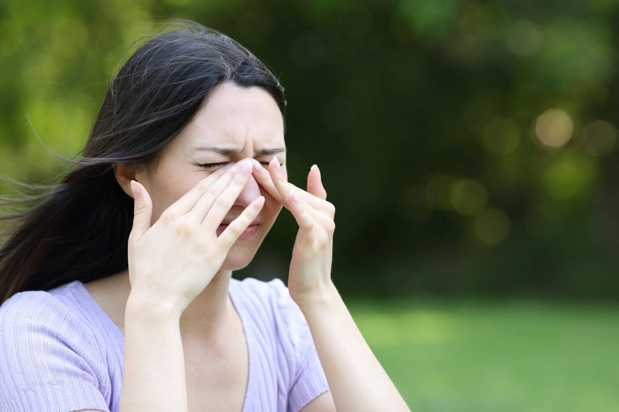 A woman experiencing sinus pressure outside, holding her nose.