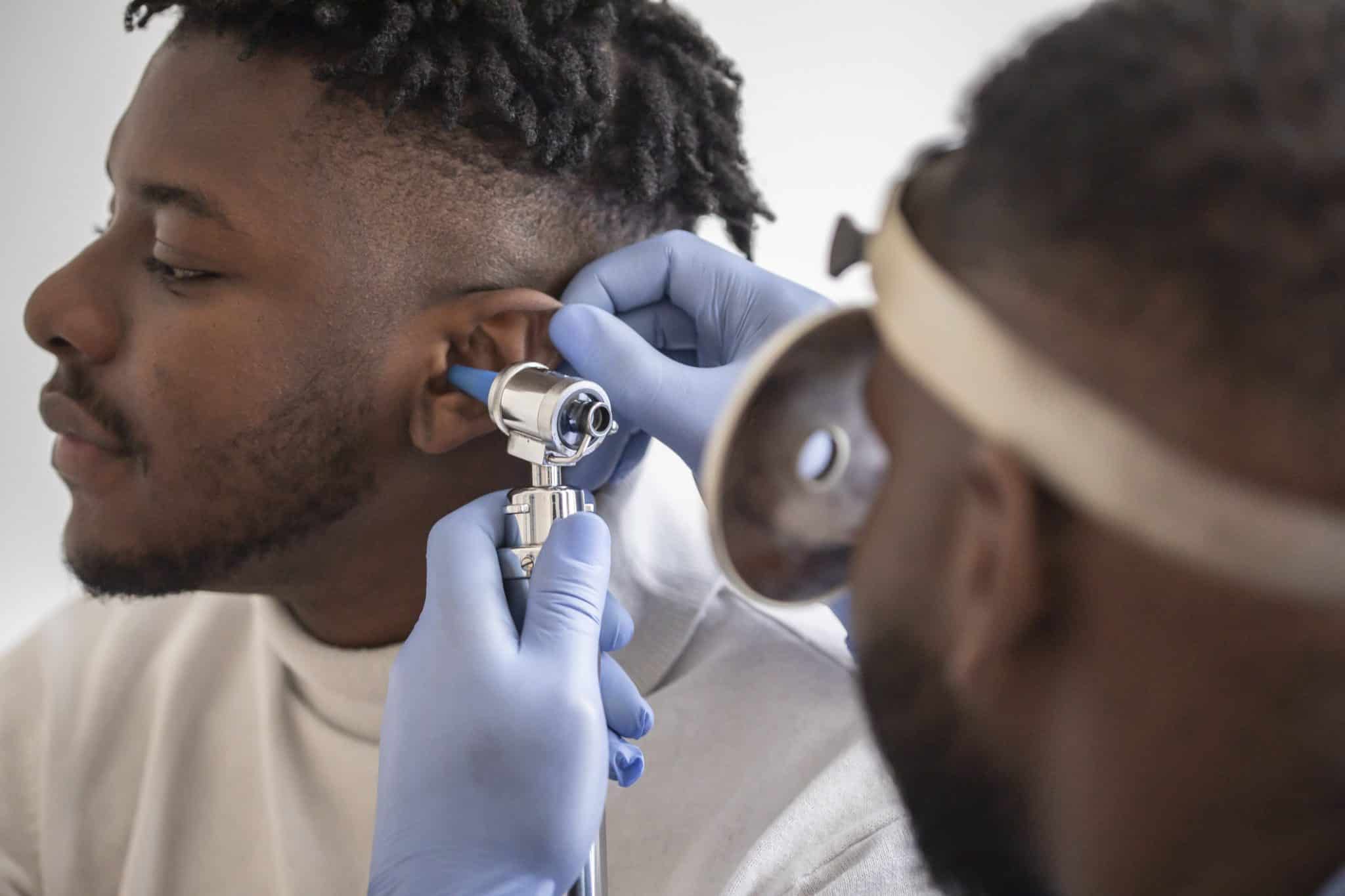 Close up of a male  doctor carefully holding the ear of his patient to establish a clearer view of the inside of his ear, to see if he requires hearing aids at a modern clinic