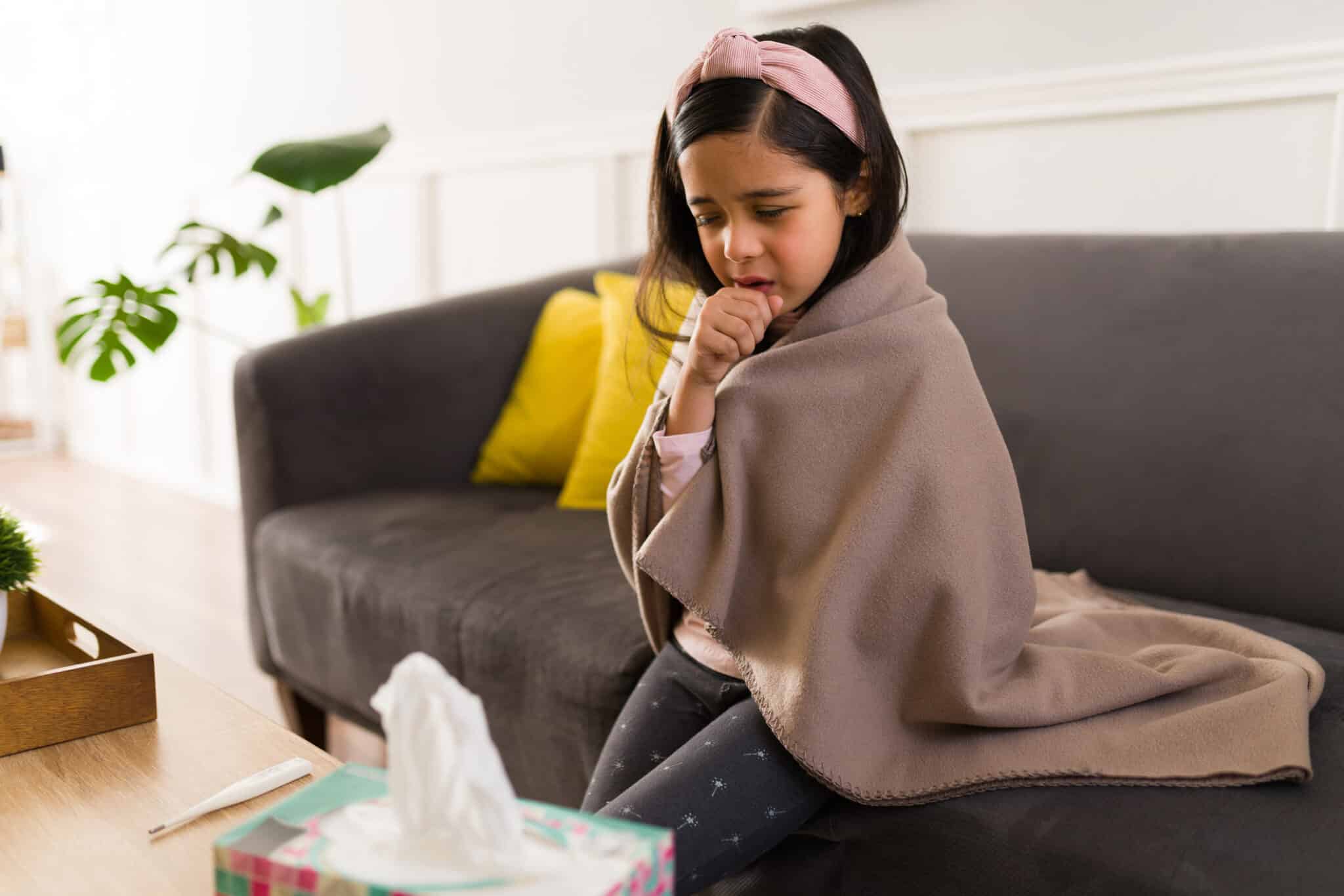 Little girl sitting on the couch and coughing.