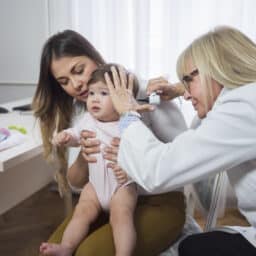 Doctor examining baby girl with Otoscope