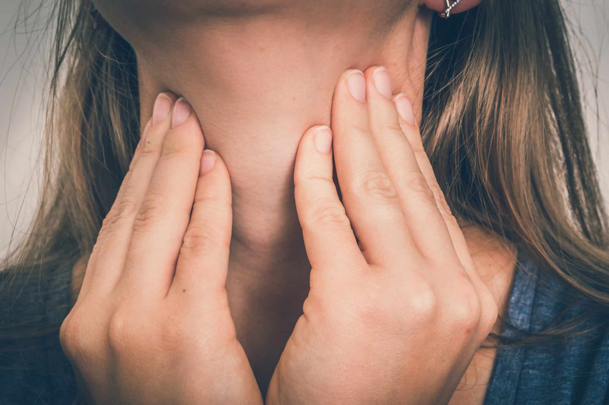 Close up of woman feeling her throat.