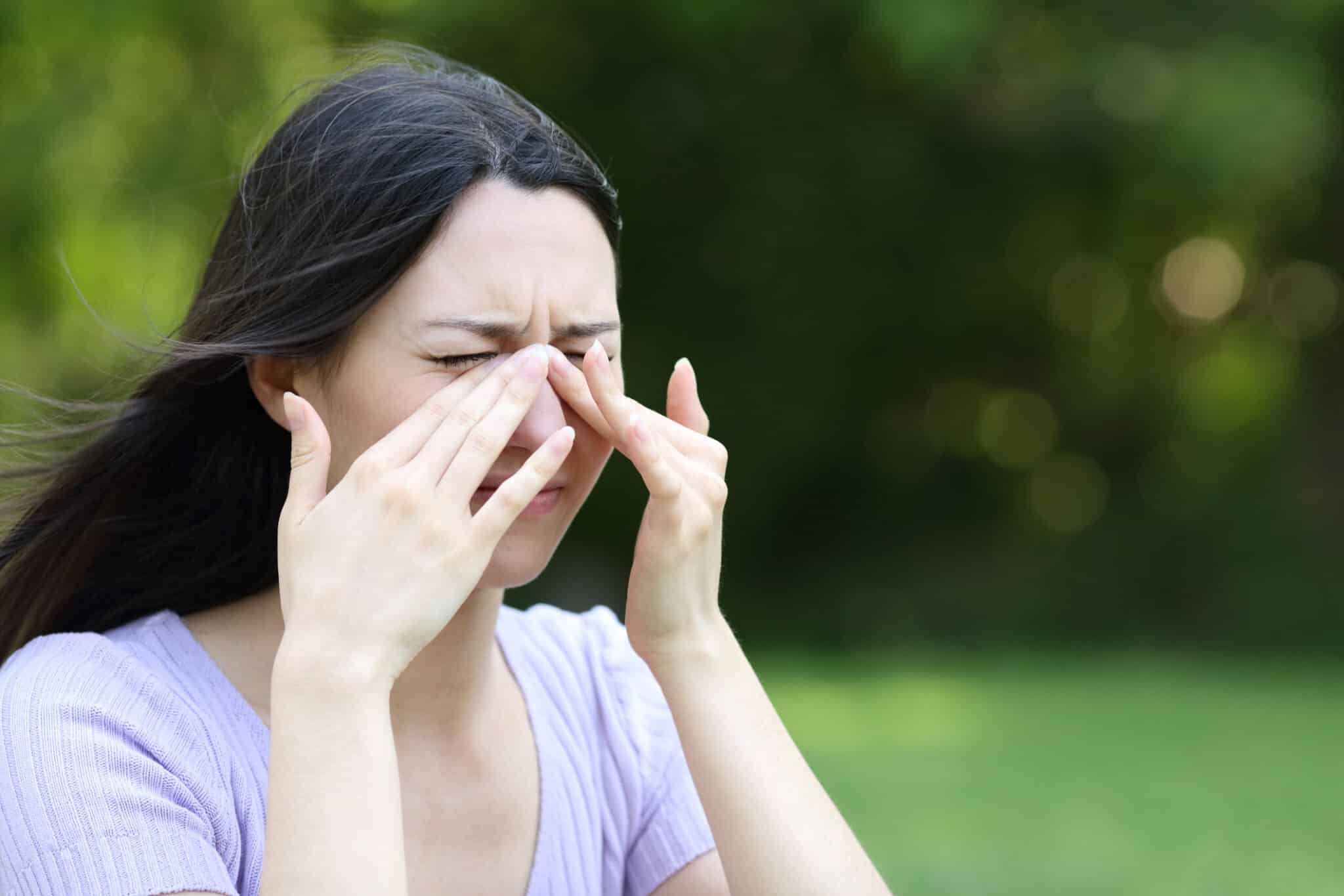 Woman scratching itchy eyes or sinus in a park