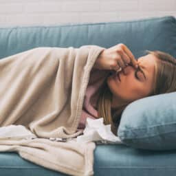 Woman with a sinus infection resting on her couch and rubbing her forehead.