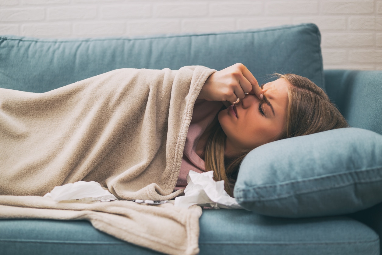 Woman with a sinus infection resting on her couch and rubbing her forehead.
