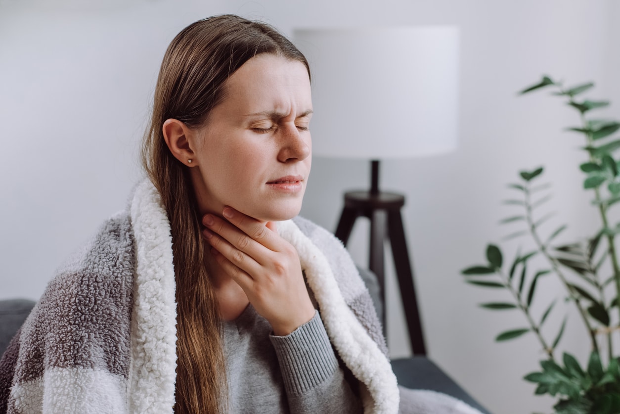 Frowning woman holding her sore throat.