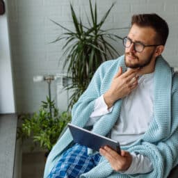 Young man using digital tablet while resting at home with a sore throat