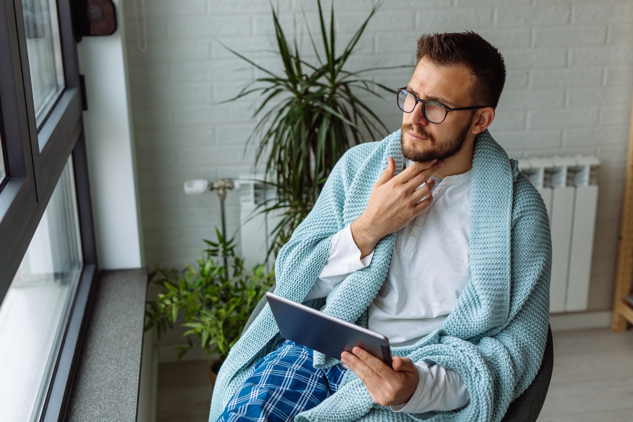 Young man using digital tablet while resting at home with a sore throat.