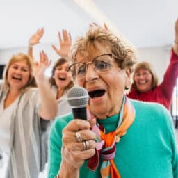 Senior woman singing karaoke with her friends.